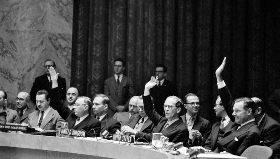 Officials at a meeting table, with some raising their hands.