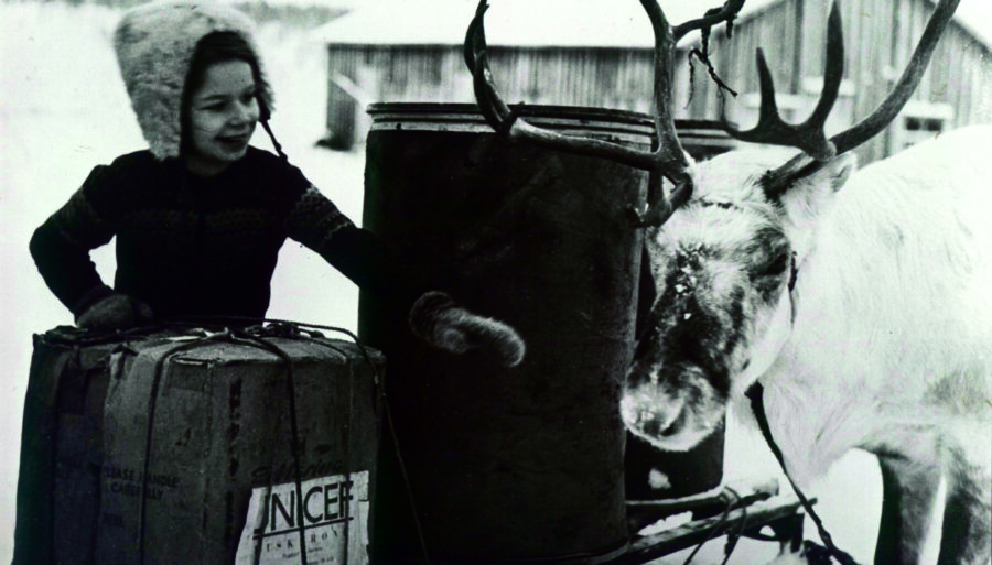 A winter photo of a young girl with a reindeer and a support package provided by UNICEF.