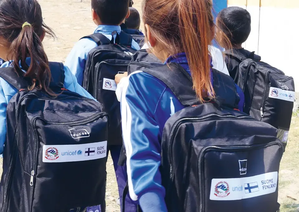 Schoolchildren wearing uniforms and carrying backpacks featuring Finnish flags and UNICEF logos.