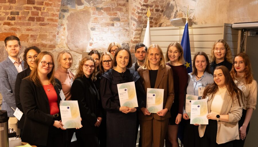 A group of young people posing for the camera with the Minister for Foreign Affairs of Finland, holding Finland’s national Youth, Peace and Security action plan.