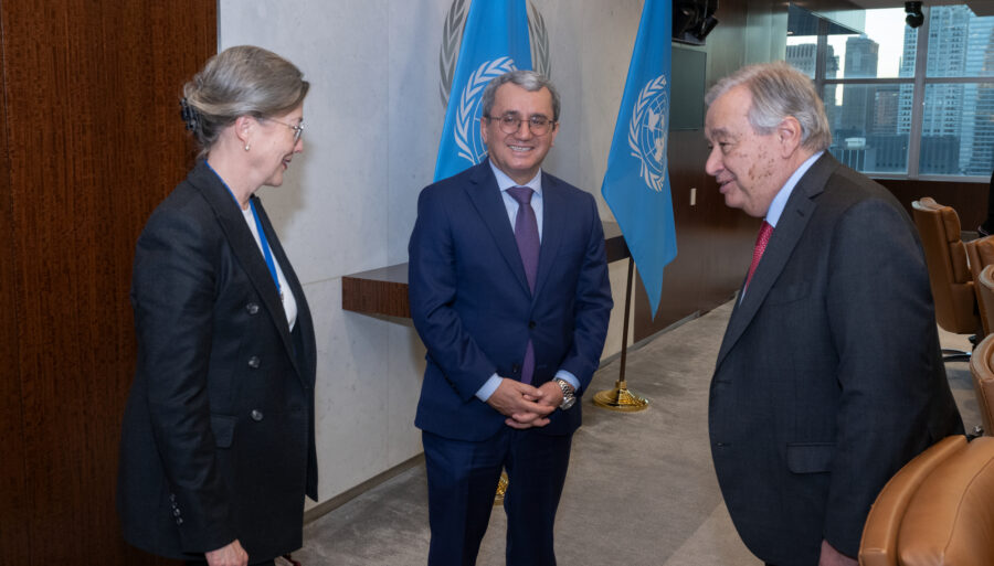 Three people interacting in the photo, with a UN flag in the background.