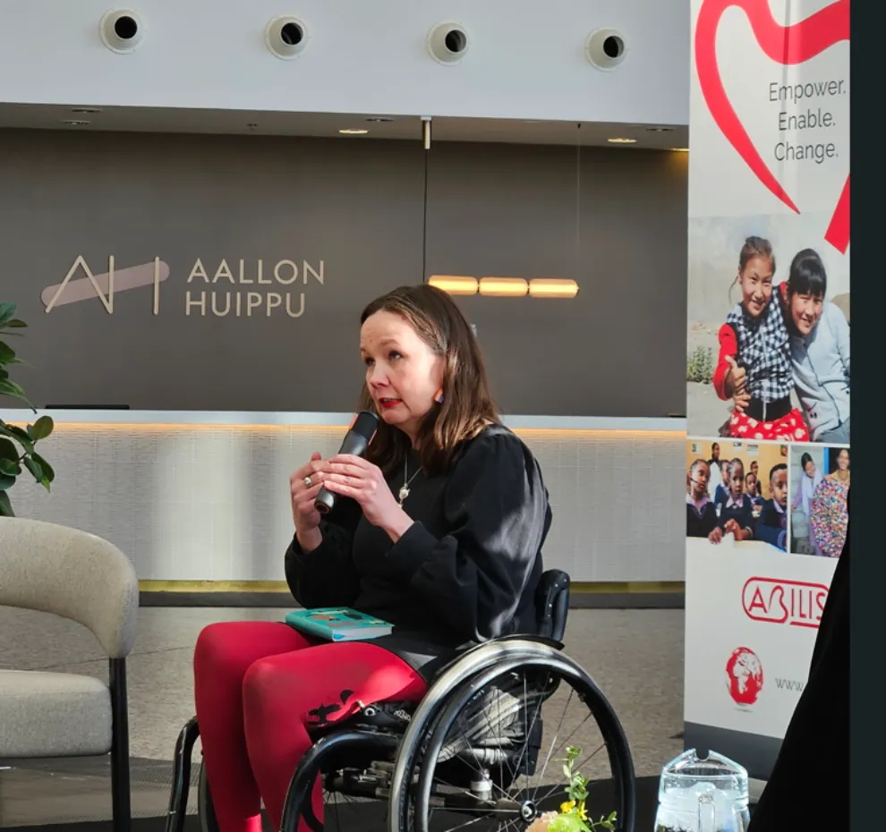 A woman in a wheelchair speaking into a microphone at a public event.